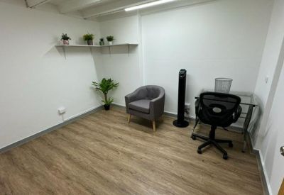 Minimalist breakout room with a grey armchair, a small desk, and potted plants.