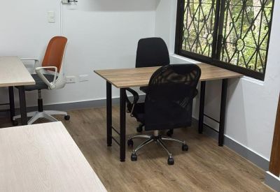 Small private office with wooden desks, a black fan, and a barred window.