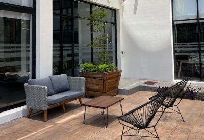 Outdoor lounge area with a grey sofa, black wire chairs, and a wooden planter.