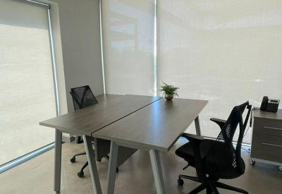 Minimalist meeting room with two connected wooden tables and a ceiling light fixture.