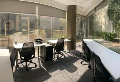 Bright coworking space with long white desks and large windows overlooking trees.