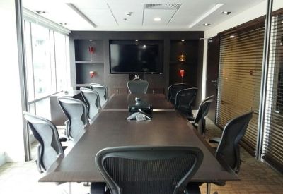 Formal boardroom with a long dark conference table, ergonomic mesh chairs, and integrated media screen.