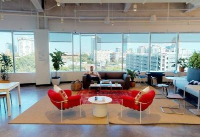 Bright communal lounge with red armchairs, city views, and indoor plants.