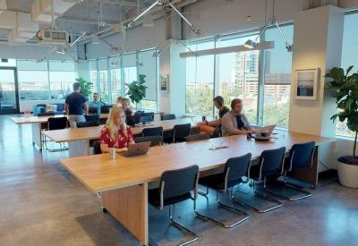 Open-plan office space with long wooden desks and large windows.
