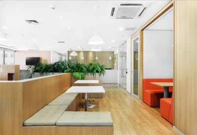 Spacious communal lounge with wooden benches, white cafe tables, and lush green plants.