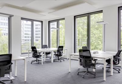 Bright open-plan workspace with white desks and black ergonomic chairs near large windows.