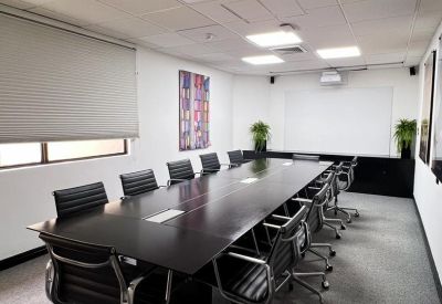 Professional boardroom with a long dark wood table, leather chairs, and a white projector screen.