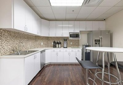 Communal kitchen area with white cabinetry, mosaic backsplash, and high-top table.