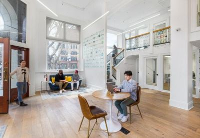 Spacious sunlit lobby with high ceilings, wood floors, and a person working at a round table.