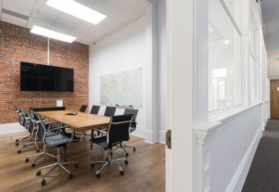 Modern conference room with a large wooden table, brick accent wall, and flat-screen monitor.