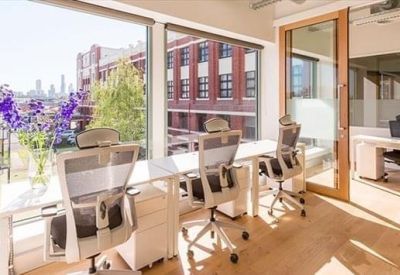 Bright, sunlit office area with white desks, ergonomic chairs, and floor-to-ceiling city views.