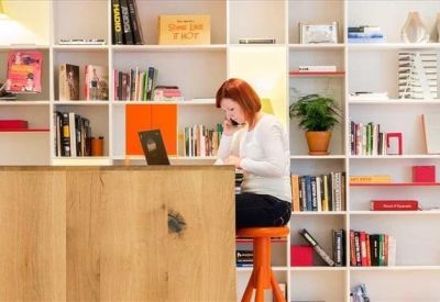 Quiet workspace with a person at a high desk in front of a large white shelving unit full of books.