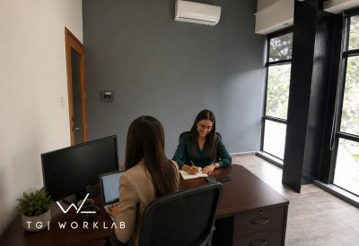 Small office meeting space with two women working at a dark wood desk under a grey accent wall.