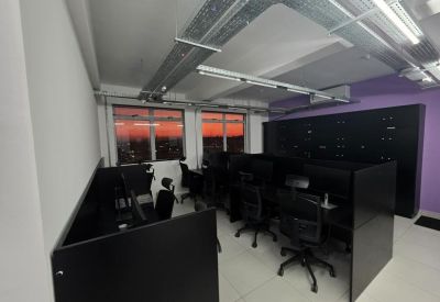 Dark office suite with several desks and a view of a sunset through the windows.