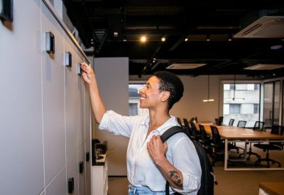 A woman smiling while opening a tall grey storage locker in a modern common area.