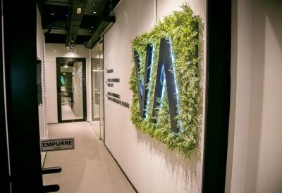 Office hallway featuring a green plant wall with an illuminated logo and glass doors.