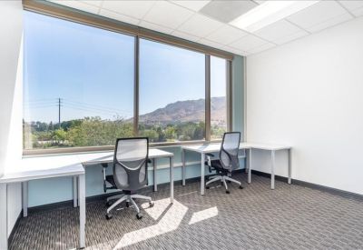 Bright corner office with two desks and large windows overlooking a mountain landscape.