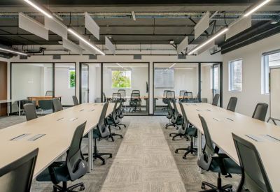 Spacious open-plan workspace with multiple rows of desks and glass-walled private offices.