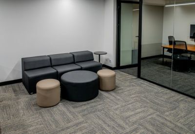 Lounge area featuring a grey sofa, round coffee table, and view into a glass-walled meeting room.