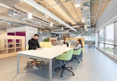 Coworking office with white desks, green ergonomic chairs, and floor-to-ceiling windows.