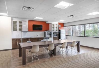 Bright communal kitchen and breakroom with a long wooden dining table and orange wall.