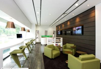 Contemporary business lounge with green armchairs and dark wood paneling.
