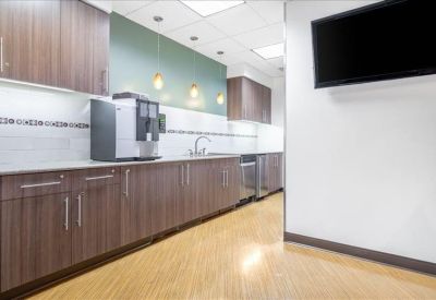 Modern office kitchen with dark wood cabinetry, coffee machine, and wood-style flooring.