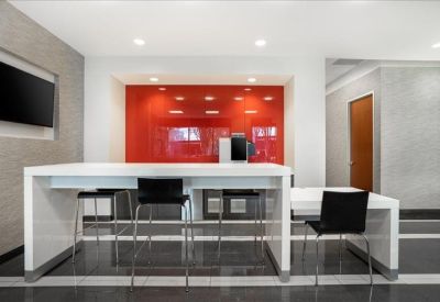 Office kitchen area with a high white table and vibrant red backsplash.