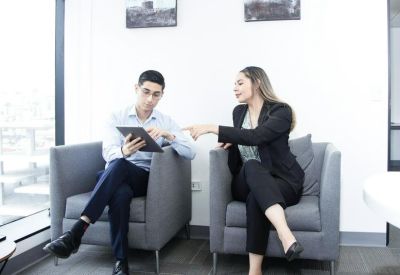 Two colleagues discussing work on a tablet in comfortable grey armchairs.