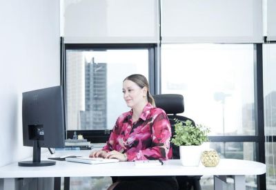 Professional woman working at a white desk in a bright office with city views.