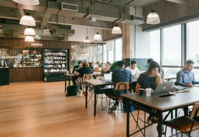 Sun-drenched coworking space with people working at wooden tables near large windows.
