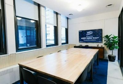 Bright conference room with a large wooden table and a wall-mounted digital display.