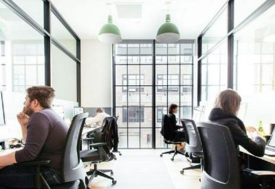 Modern open-plan office with glass partitions, ergonomic chairs, and industrial windows.