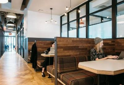 Cozy wooden booth seating area with people working on laptops and a bright corridor.