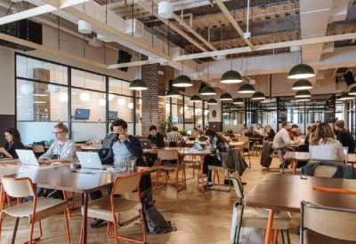 Spacious coworking hub with wooden tables, pendant lighting, and multiple people working.