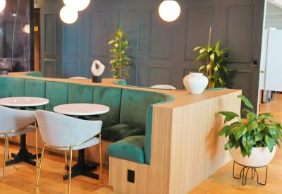 Lounge area with a curved velvet booth, white marble tables, and hanging globe lights.