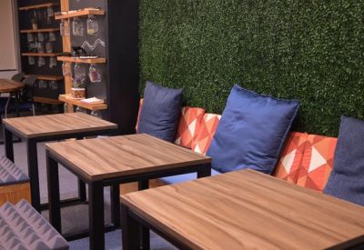 Communal lounge area with wooden tables, blue cushions, and a green plant wall.