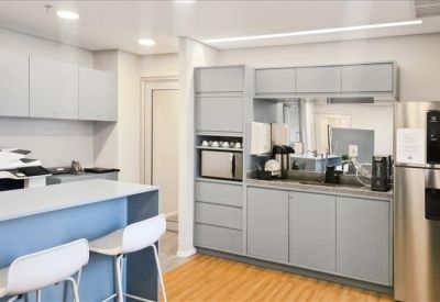 Modern communal kitchen with grey cabinetry, breakfast bar, and stainless steel fridge.