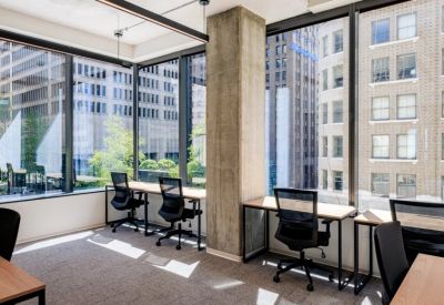 Bright open-plan workspace with multiple desks facing large windows with city views.