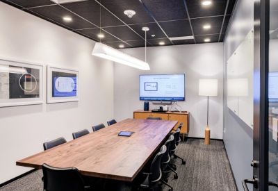 Professional conference room featuring a long wooden table, black chairs, and a wall-mounted screen.