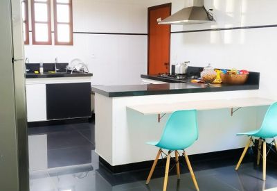Modern kitchen and dining area with teal chairs and polished black floors.