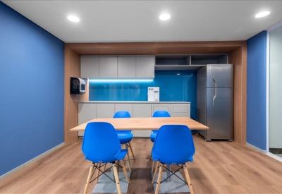 Modern communal kitchen and dining area with blue walls and bright blue chairs.