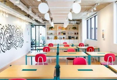 Bright open-plan office with wooden desks, pink chairs, and wall art.
