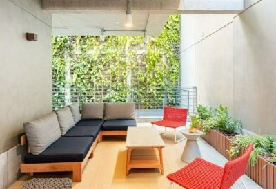 Outdoor balcony lounge with wooden seating, red chairs, and lush green plants.