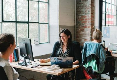Bright open-plan workspace with wooden desks and large windows overlooking trees.