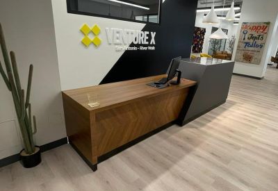 Modern reception area with a wood-fronted desk and branded black and white wall.
