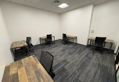 Private team office with four industrial-style desks and dark carpeting.