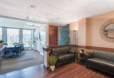 Waiting area with black leather sofas, wooden flooring, and a round wall mirror.