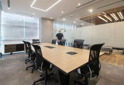Spacious boardroom featuring a large wooden table, mesh chairs, and a glass-enclosed whiteboard area.
