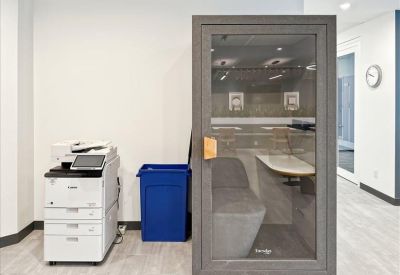 A modern, acoustic privacy pod for phone calls next to a printer and blue recycling bin.